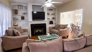 A living room with a fireplace, a ceiling fan, and a television.