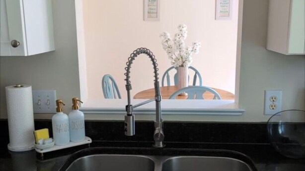 A kitchen with a modern faucet, a window with a view of a dining area, and a countertop with a soap dispenser and a sponge.