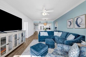 A living room with a sectional sofa, ottomans, a TV stand, and artwork on the walls.