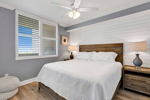 A bedroom with a bed, a ceiling fan, a nightstand with a lamp, a window with blinds, and a picture on the wall. - 19th Floor Oceanfront View at The Beach Club (Gulf Shores)