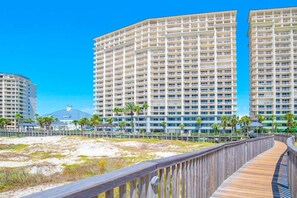 A beachfront hotel with multiple high-rise buildings, a wooden boardwalk, and palm trees.