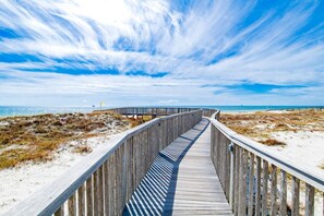 A wooden boardwalk leading to a beach with a clear sky.