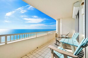 A balcony with a view of the sea, a table, and two chairs.
