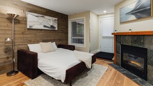 Une chambre à coucher avec un lit, une cheminée, un mur en bois et une fenêtre avec des stores.