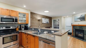 Une cuisine moderne avec des meubles en bois, des appareils électroménagers en acier inoxydable, un plan de travail en granit et une cheminée.