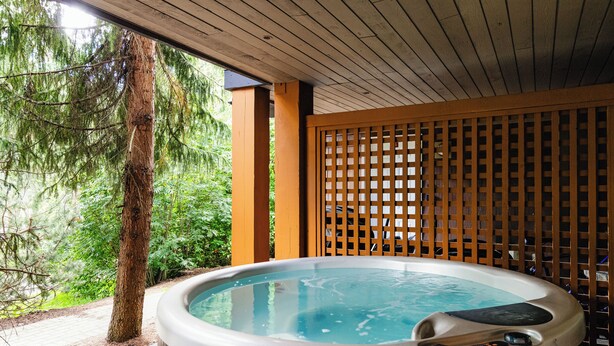 Un bain à remous avec une terrasse en bois et une clôture en bois, entouré d’arbres.