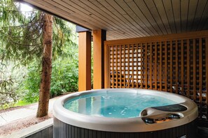 A hot tub with a wooden deck and a wooden fence, surrounded by trees.