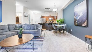A modern living room with a gray sofa, a wooden coffee table, and a dining area with a white table and chairs. - Executive| King Bed Suite / Monthly Rentals (Edmonton)