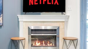 A modern living room with a fireplace, a television mounted above it, and two wooden stools. - Executive| King Bed Suite / Monthly Rentals (Edmonton)