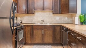 A modern kitchen with dark wooden cabinets, stainless steel appliances, and a tiled backsplash. - Executive| King Bed Suite / Monthly Rentals (Edmonton)