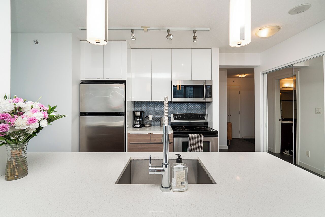 A modern kitchen with stainless steel appliances, a white countertop, and a vase of flowers.