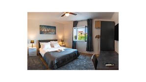 Une chambre à coucher comprenant un lit, des tables de chevet, un ventilateur de plafond, une fenêtre avec des rideaux, un téléviseur et un lampadaire.
