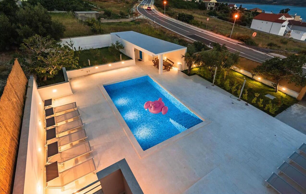 Ein moderner Poolbereich mit einem klaren, blauen Pool, einer Flamingo-Deko und einer Treppe zu einer erhöhten Ebene.