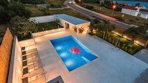 Une piscine sur le toit, dotée d’un jacuzzi, entourée d’un ensemble architectural moderne offrant une vue sur une route et des bâtiments éloignés.