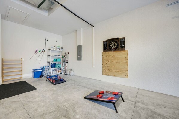 A room with a dartboard, shelves with various items, and a table with a board game. - New Luxury 5BR Gulf-Access Heated Pool & Spa Home Dock w/ Boat Cleats, Sleeps 13 (Cape Coral)