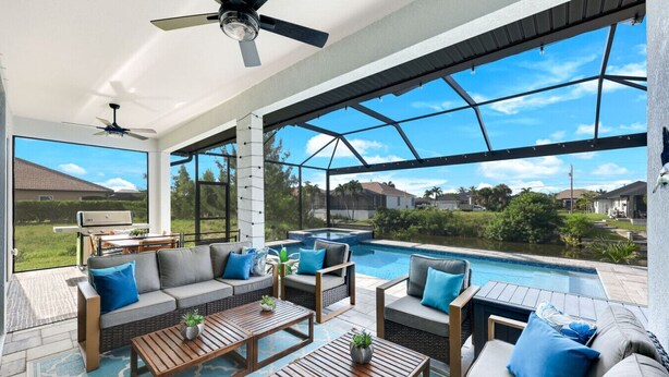 A spacious outdoor living area with a pool, seating, and a ceiling fan. - New Luxury 5BR Gulf-Access Heated Pool & Spa Home Dock w/ Boat Cleats, Sleeps 13 (Cape Coral)