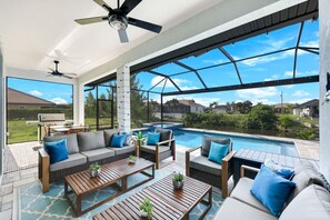 A spacious outdoor living area with a pool, seating, and a ceiling fan. - New Luxury 5BR Gulf-Access Heated Pool & Spa Home Dock w/ Boat Cleats, Sleeps 13 (Cape Coral)