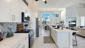 A modern kitchen with white cabinets, a central island, and a dining area with a view of the outdoors.