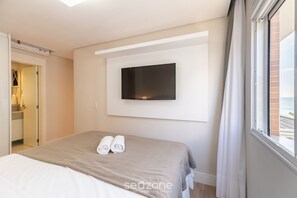 A hotel room with a bed, a flat-screen TV mounted on the wall, and a window with curtains.
