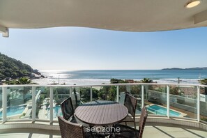 A balcony with a view of the ocean, a pool, and outdoor furniture.