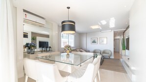 Una cocina moderna con una mesa de vidrio, sillas blancas y una lámpara colgante negra.