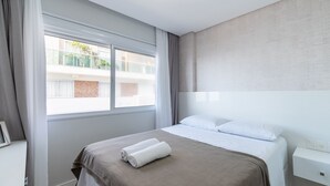Una habitación de hotel moderna con una cama grande, una mesita de noche y un ventanal con cortinas.