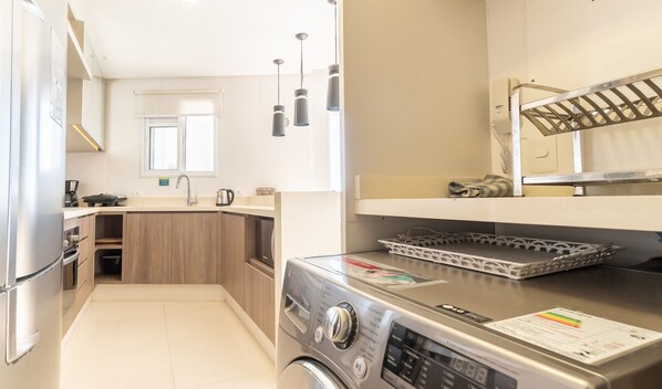 Una cocina compacta con lavadora, cafetera y tetera.
