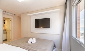A hotel room with a bed, a flat-screen TV mounted on the wall, and a window with curtains.