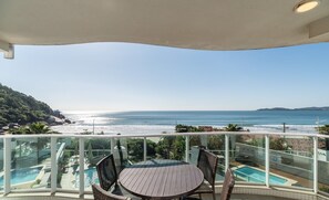 Un balcón con vistas al océano, una piscina y mobiliario exterior.