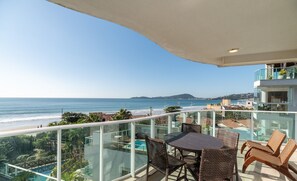 A balcony with a glass railing overlooking a beach and ocean.