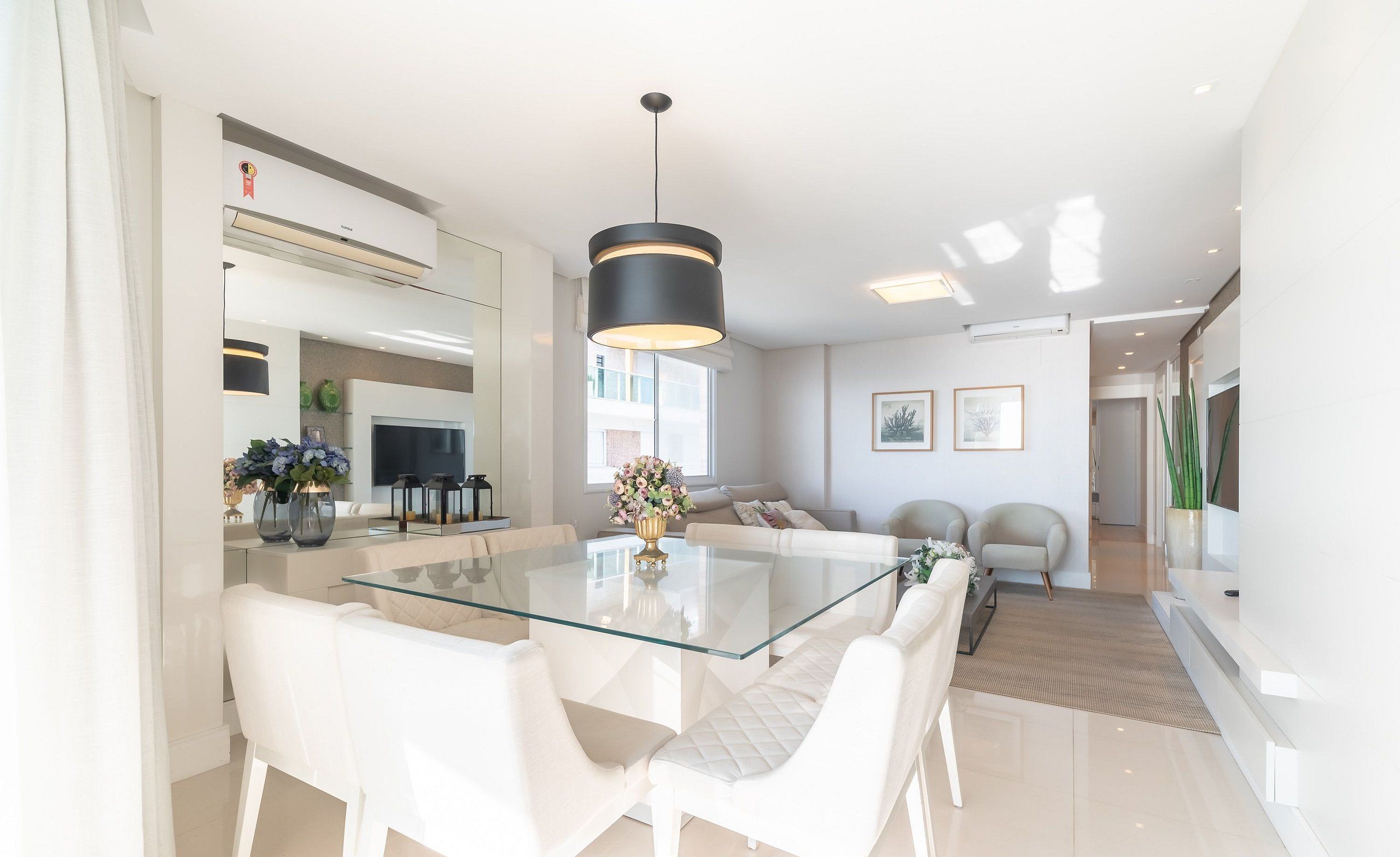 Una cocina moderna con una mesa de vidrio, sillas blancas y una lámpara colgante negra.