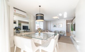 Una cocina moderna con una mesa de vidrio, sillas blancas y una lámpara colgante negra.