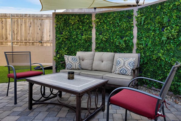 Un patio exterior con un sofá, dos sillones y una mesa.