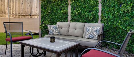 Een terras met een bank, twee stoelen, een tafel en een decoratieve wand.
