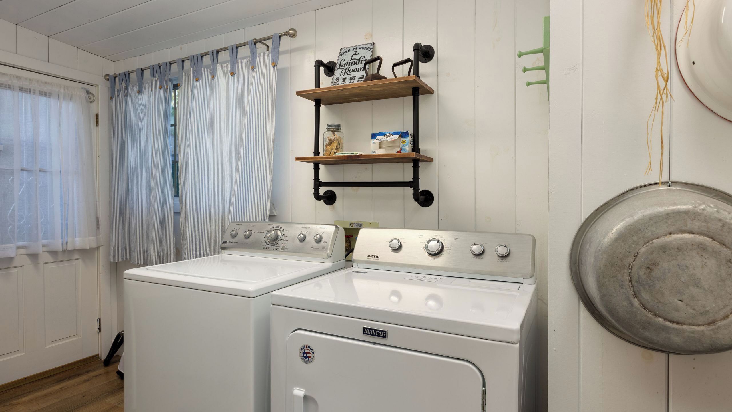 A laundry room with two Maytag washers, a shelf with laundry supplies, and a sign indicating it's open 24 hours.