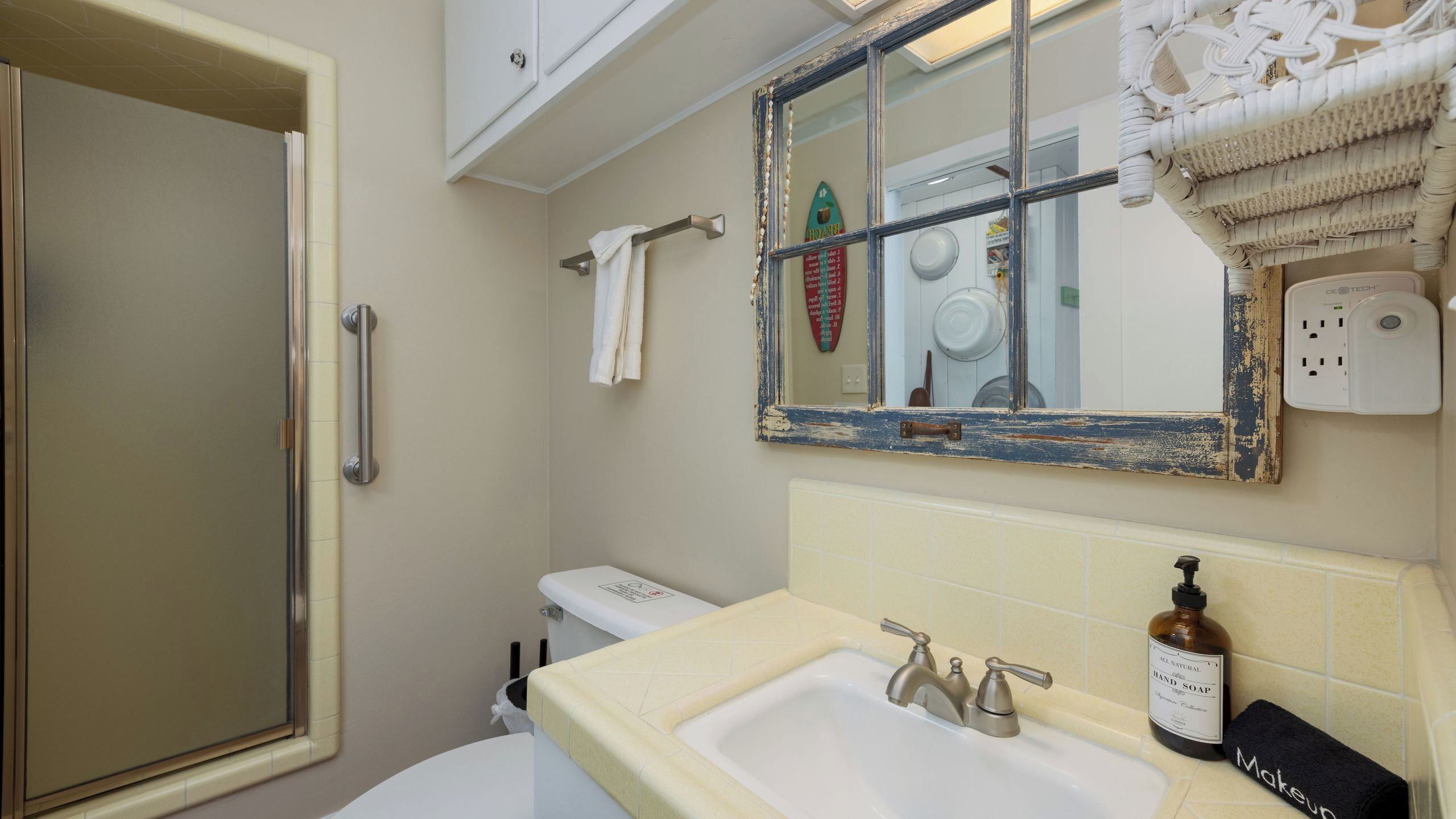 A bathroom with a shower, toilet, sink, and a mirror with a decorative frame.