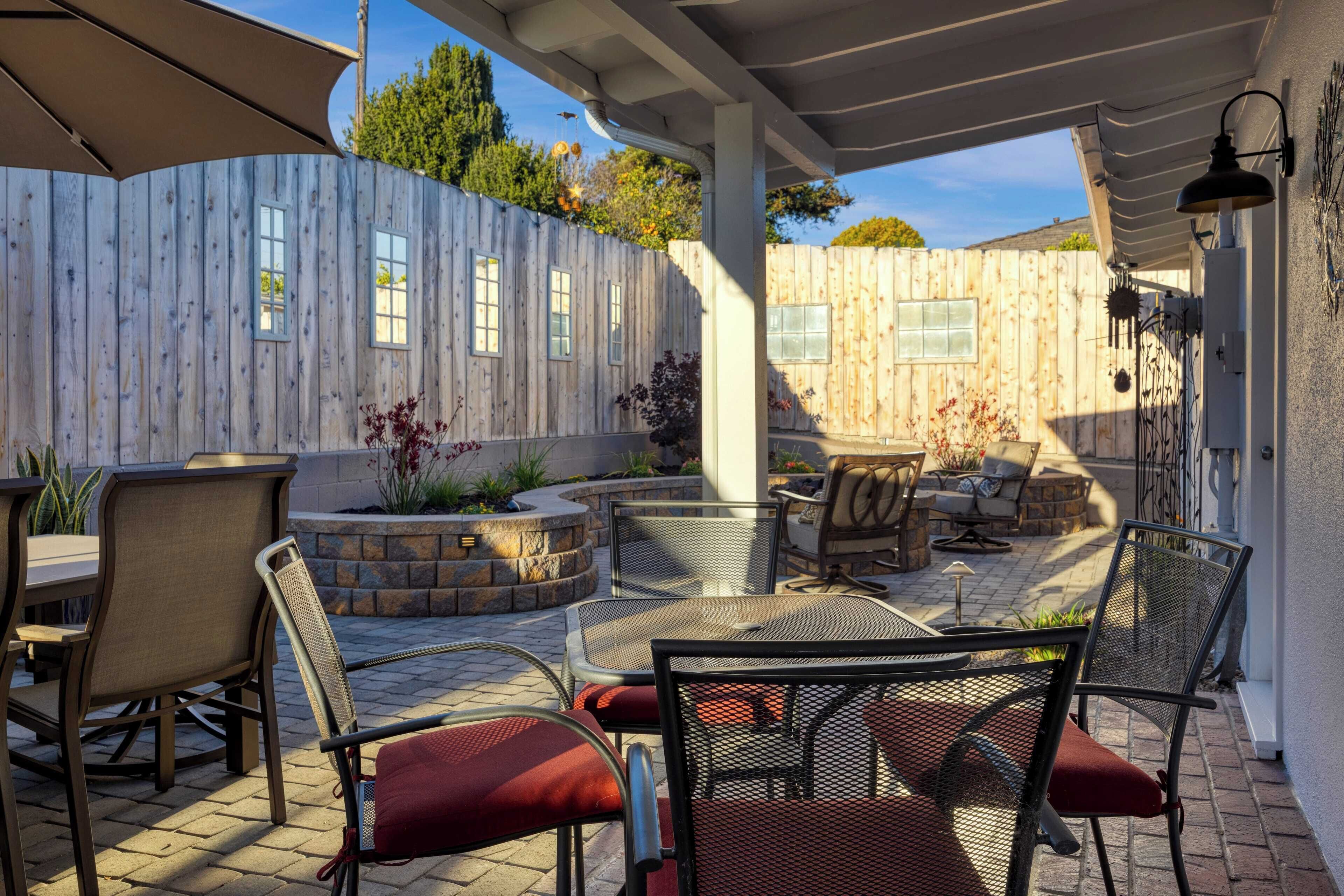 Un patio al aire libre con cerramiento de madera, mobiliario exterior y una pérgola que proporciona sombra.