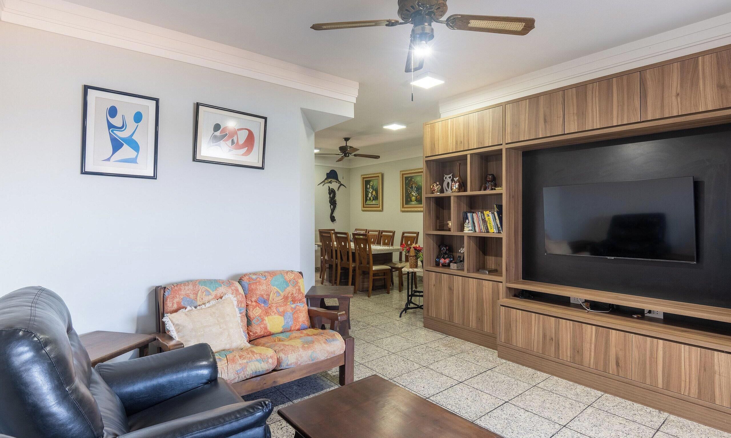 A living room with a leather sofa, a wooden coffee table, a large flat-screen TV, and a ceiling fan.