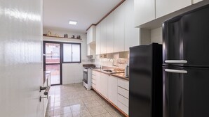 Una cucina con mobili bianchi, un frigorifero nero e una finestra con vista all'esterno.