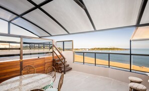 A spacious balcony with a view of the beach and ocean, wooden furniture, and a glass railing. - Penthouse With Pool and sea View - Vdi0401 (Guarapari)