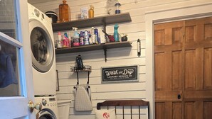 Uma lavanderia com máquina de lavar, secadora, um banco, um travesseiro de gato e uma placa para 'Wash and Dry Laundry Service Co'.