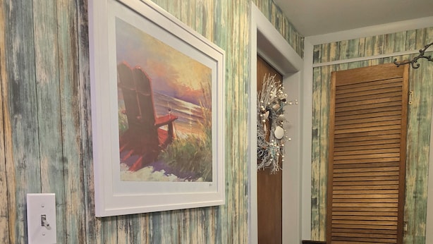 Um corredor com design rústico na parede, um quadro emoldurado, uma porta de madeira com uma grinalda decorativa e um interruptor de luz.