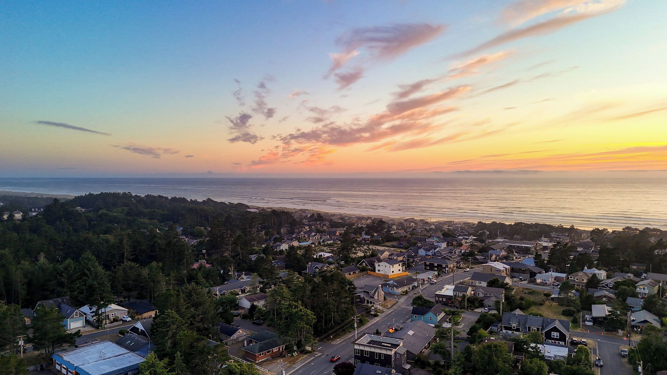 Un quartier résidentiel situé sur la côte, avec des maisons, des routes et une vue sur l’océan au coucher du soleil.
