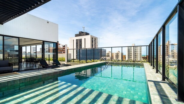En pool på taget med krystalklart vand, omgivet af moderne bygninger og en klar himmel.