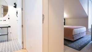 A bedroom with a bed, a bedside table, a mirror, and a window. - Your Lisbon Escape: Modern Apartment in Prime Historic Location (Lisboa)