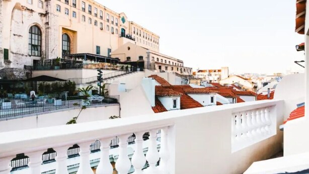 Ein Gebäude mit einem Glockenturm, einem Balkon mit weißen Brüstungen und roten Ziegeldächern im Hintergrund.