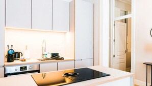 Una cocina moderna con armarios blancos, horno empotrado y encimera con hervidor y tostadora.