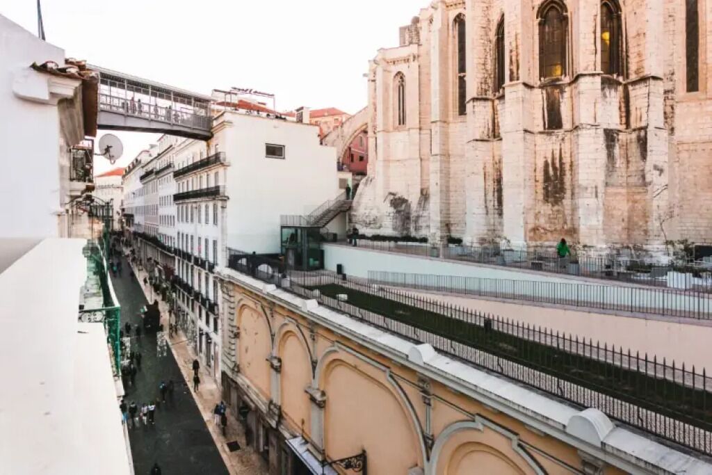 Un edificio histórico con una fachada destacada, un puente peatonal y una calle debajo.