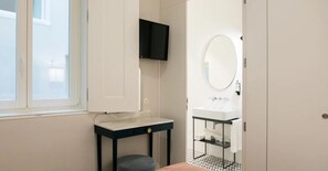 Une salle de bain avec un lavabo blanc, un miroir et un téléviseur fixé au mur.