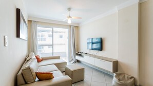 A modern living room with a sofa set, a television mounted on the wall, and a ceiling fan.